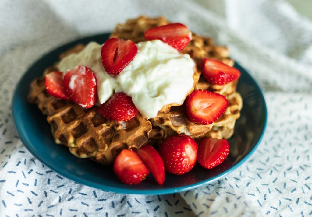 a blue plate topped with waffles covered in whipped cream and strawberries